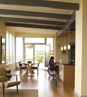 A person in a wheelchair near a kitchen counter in a large open plan living/dining area.