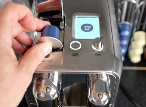 a hand places a coffee pod into a coffee making machine.